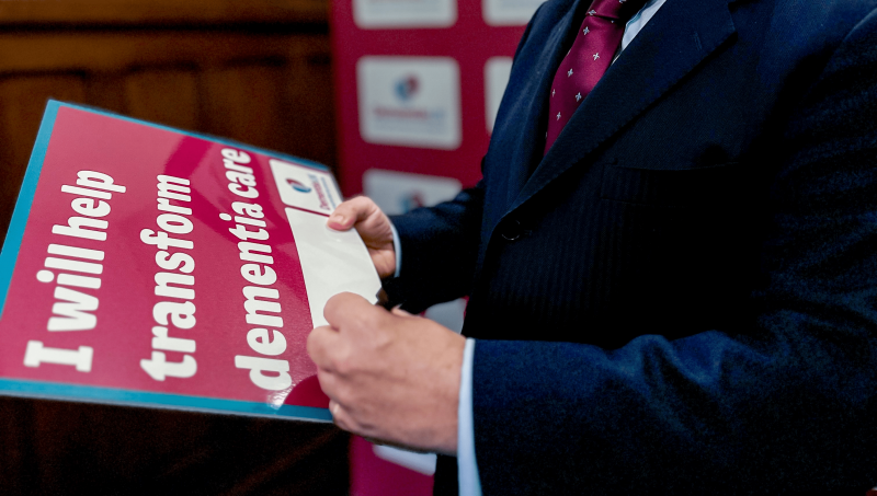 A politician holding 'I pledge to make dementia care fairer' sign and writing their name on it